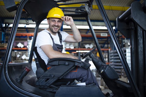 Portrait of smiling professional forklift driver in factory's warehouse.